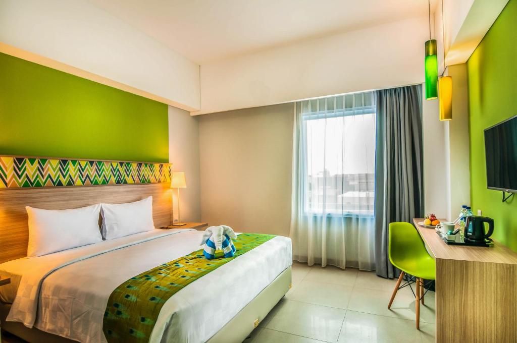 Habitación de hotel con cama, escritorio, silla, televisor y ventana con cortinas.