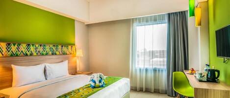 Habitación de hotel con cama, escritorio, silla, televisor y ventana con cortinas.