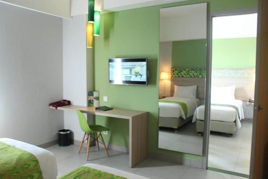 A hotel room with a bed, a desk with a chair, a television, and a mirror.