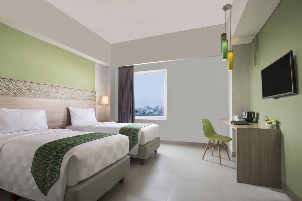 Habitació d'hotel amb dos llits, un escriptori, una cadira, una televisió i una finestra amb vista a la ciutat.