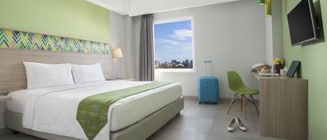 Habitación de hotel con cama, escritorio, televisor, maleta y vistas a la ciudad.