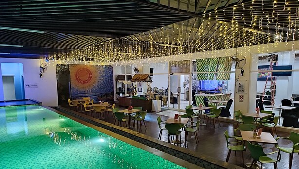 An indoor swimming pool with a tiled floor, surrounded by green chairs and tables, and a ceiling with hanging lights. - Khas Makassar  (Makassar)