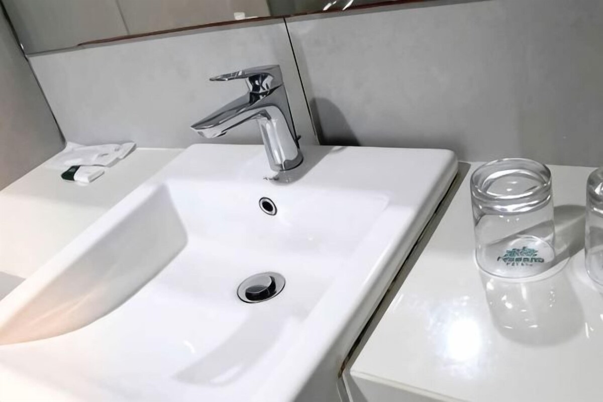 A white bathroom sink with a modern faucet, a glass soap dispenser, and a clear glass with a label.
