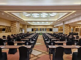 Una sala conferenze con file di tavoli e sedie, un palco con un leggio e uno schermo grande.