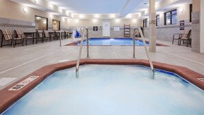 A hotel pool area with a hot tub, lounge chairs, and a changing room.
