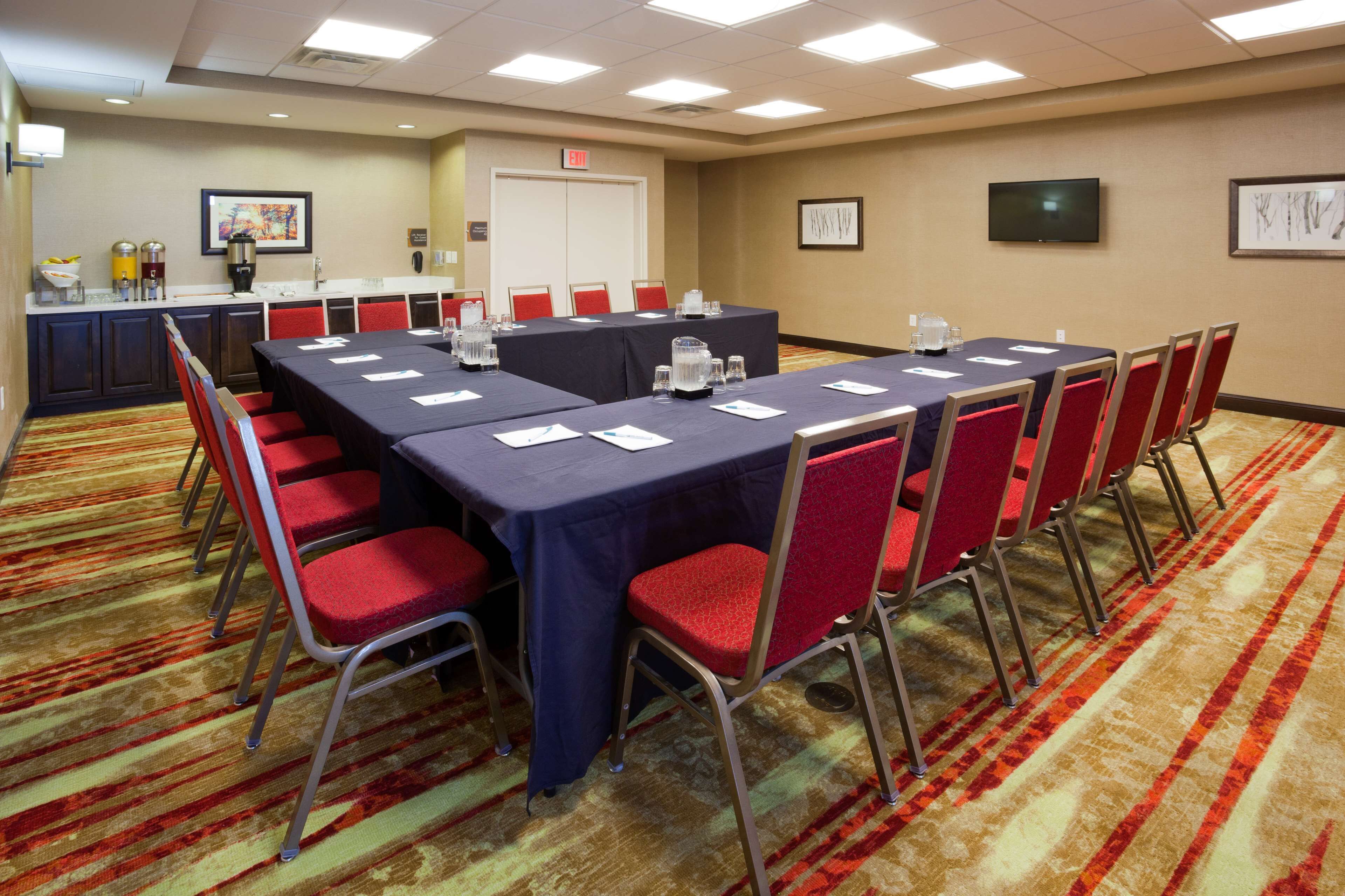 Un salón de conferencias con una larga mesa, sillas rojas y piso alfombrado.