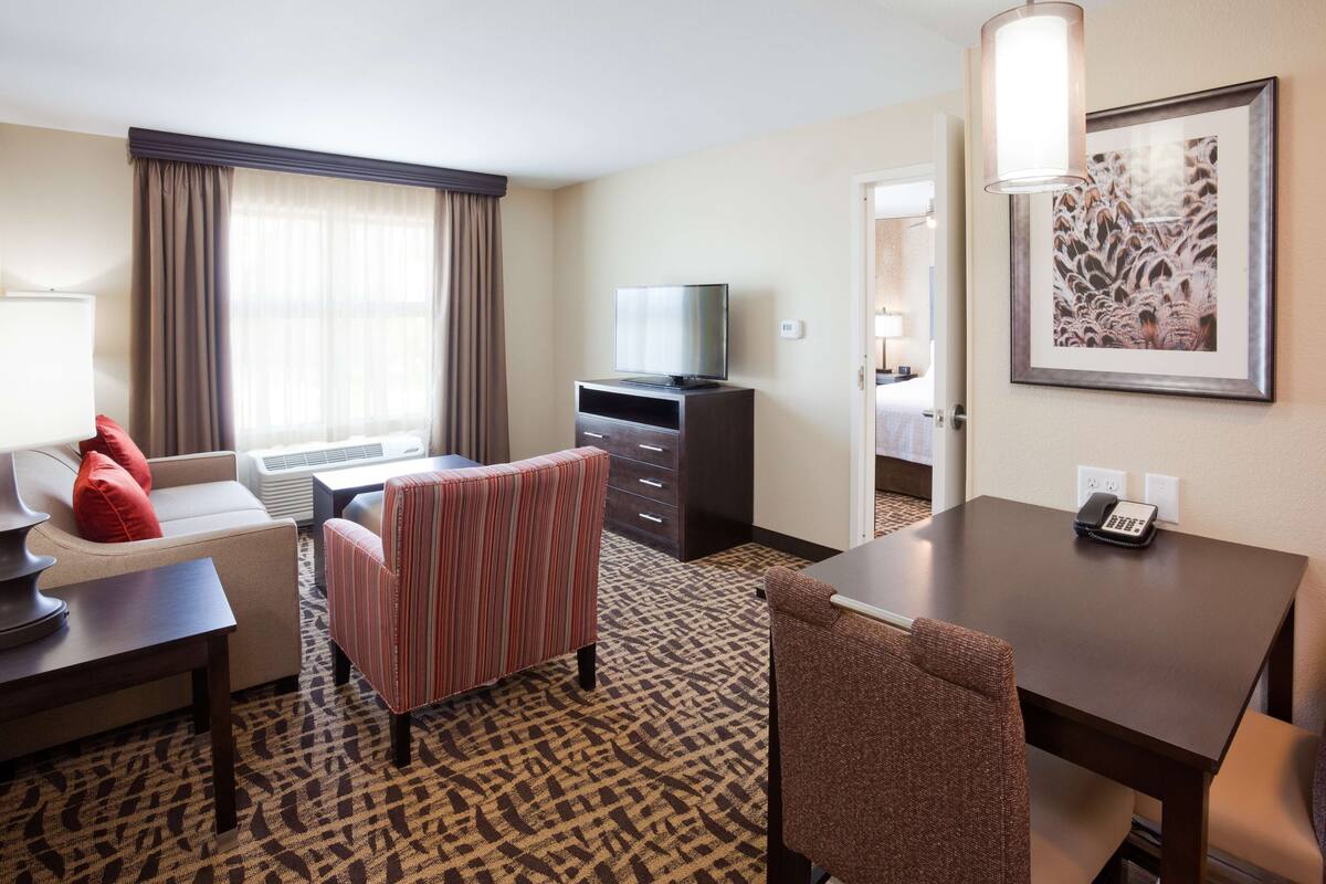 A hotel room with a sofa, a striped chair, a desk, a television, a framed picture on the wall, and a patterned carpet.