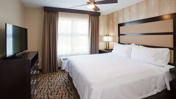 A hotel room with a large bed, a television on a dresser, a ceiling fan, and a window with curtains.