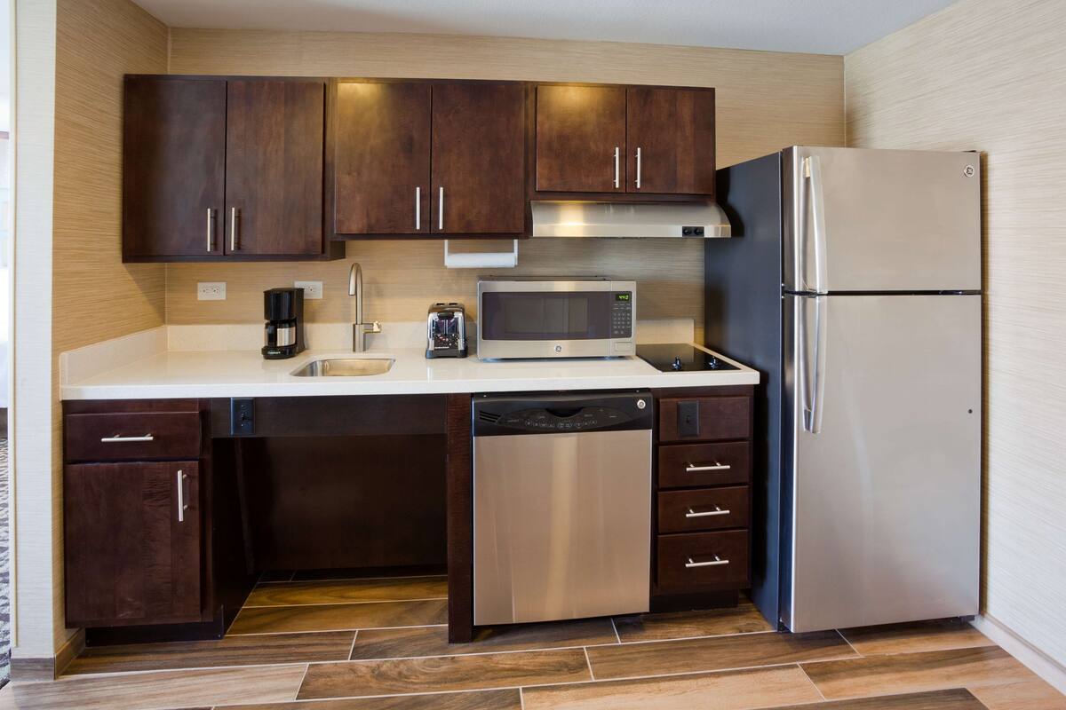 A modern kitchen with dark wooden cabinets, stainless steel appliances, and a tiled floor.