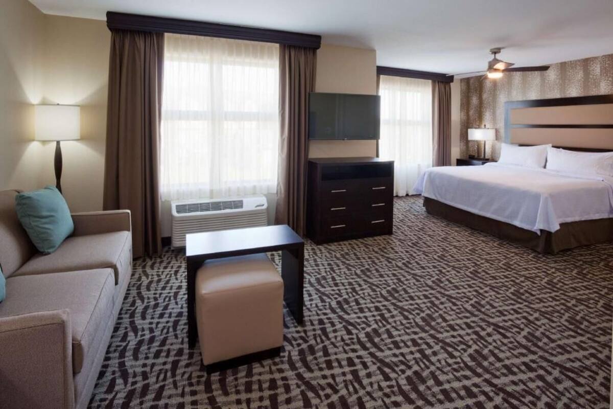 A hotel room with a bed, a TV, a desk, a chair, and a sofa.
