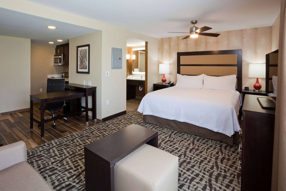 A hotel room with a bed, desk, chair, and a small table.