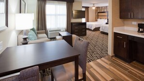 A hotel room with a dining area, a bed, a TV, a desk, and a kitchenette.