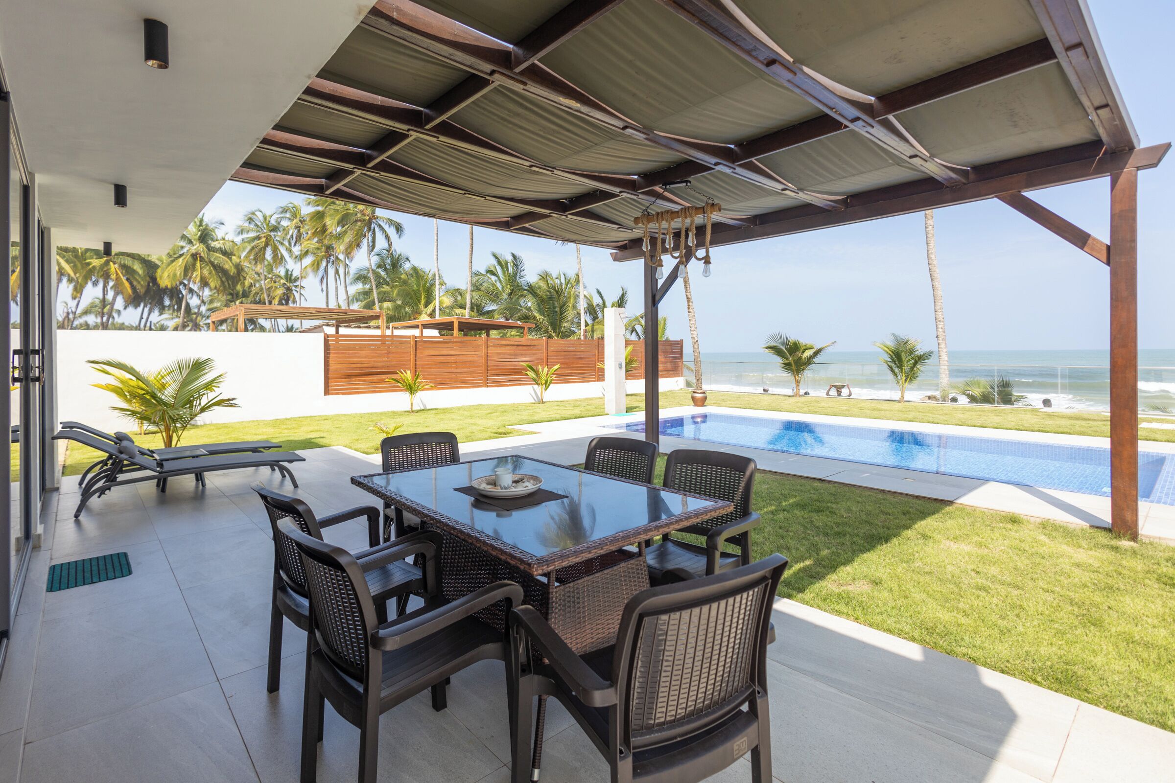 Un patio techado con piscina, mobiliario exterior y vista al océano.