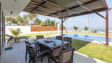 Un patio techado con piscina, mobiliario exterior y vista al océano.