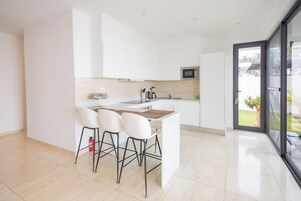 A modern kitchen with white cabinets, a central island with stools, and a view through a glass door to an outdoor area.
