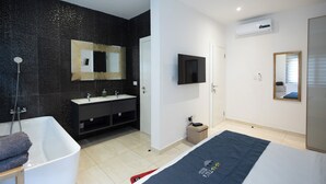 A modern bathroom with a bathtub, a vanity with a mirror, and a television mounted on the wall. - Tills Beach Hotel (Gomoa Fetteh)