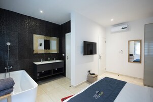 A modern bathroom with a bathtub, a vanity with a mirror, and a television mounted on the wall.
