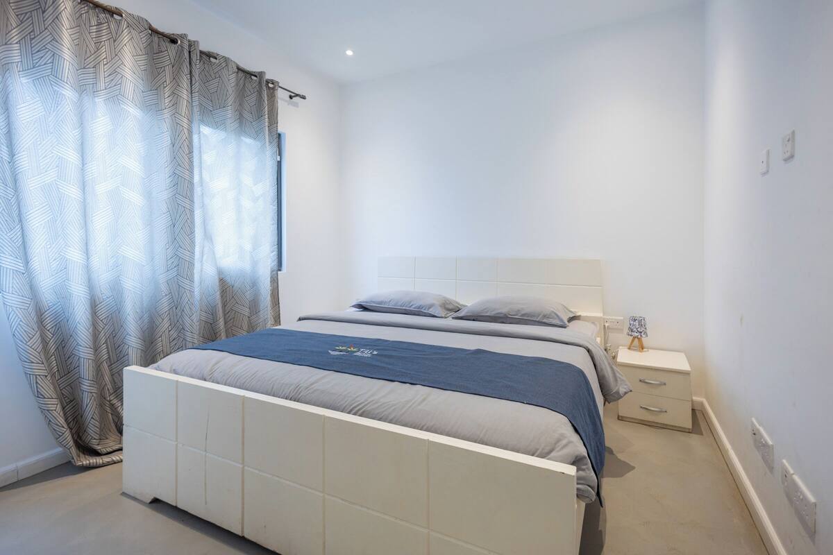 Ein Schlafzimmer mit einem Bett, einem Nachttisch und einem Fenster mit Vorhängen.