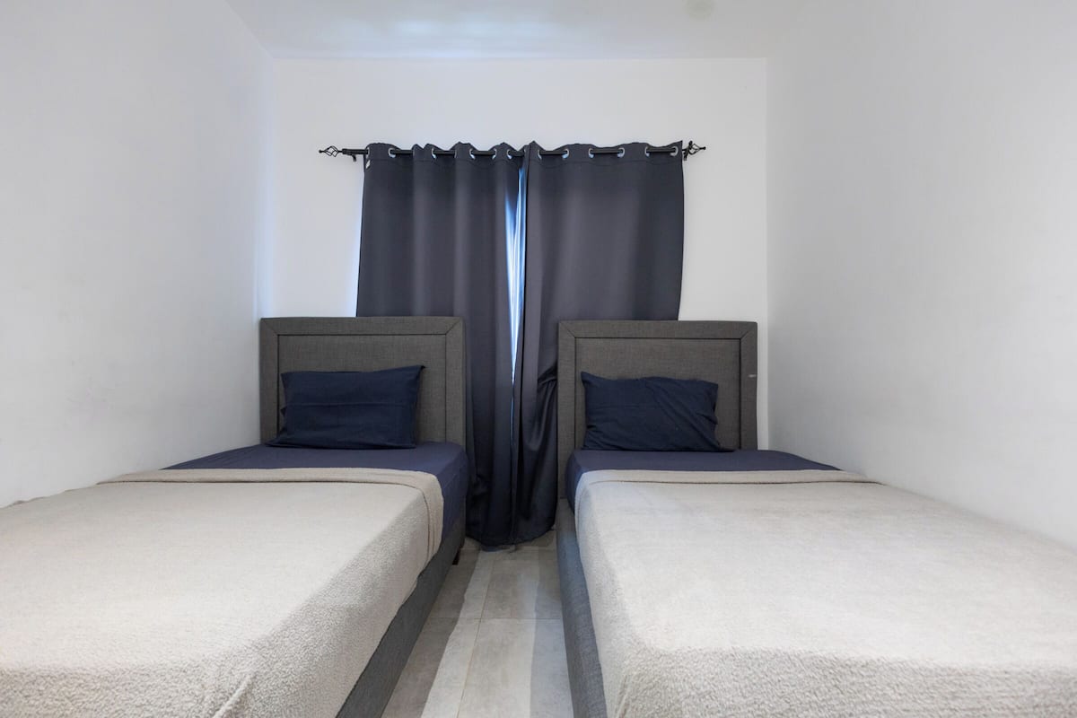 Ein Zimmer mit zwei Einzelbetten, einem dunklen Vorhang und einem schlichten, klaren Design.