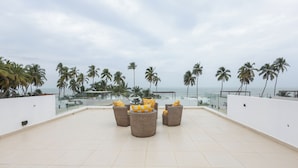 A rooftop terrace with wicker furniture and a view of palm trees and the ocean. - Tills Beach Hotel (Gomoa Fetteh)