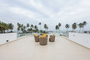 Terraço no telhado com móveis de vime e vista para palmeiras e o oceano.