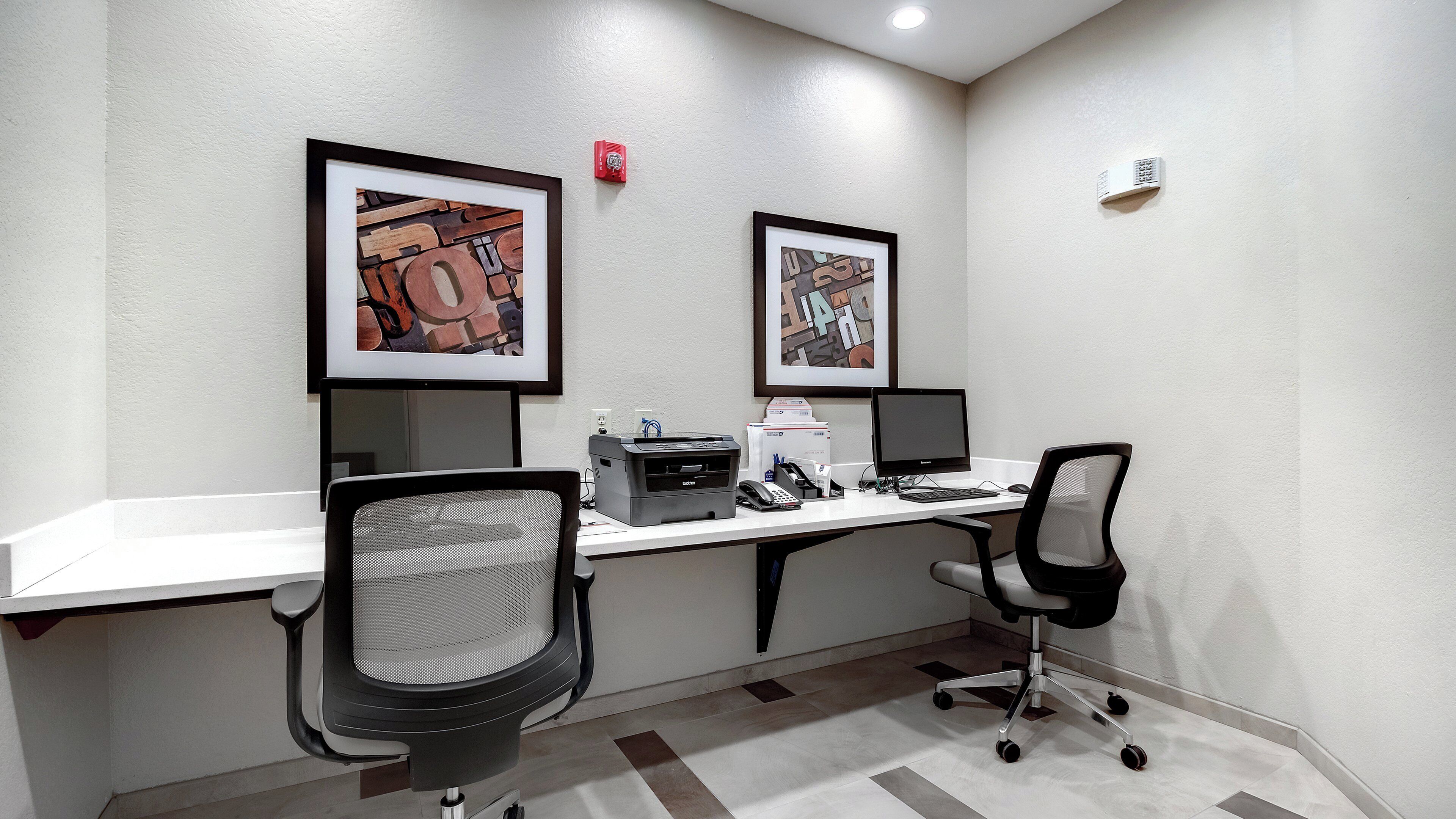 A conference room with two desks, chairs, a printer, and framed artwork on the wall.