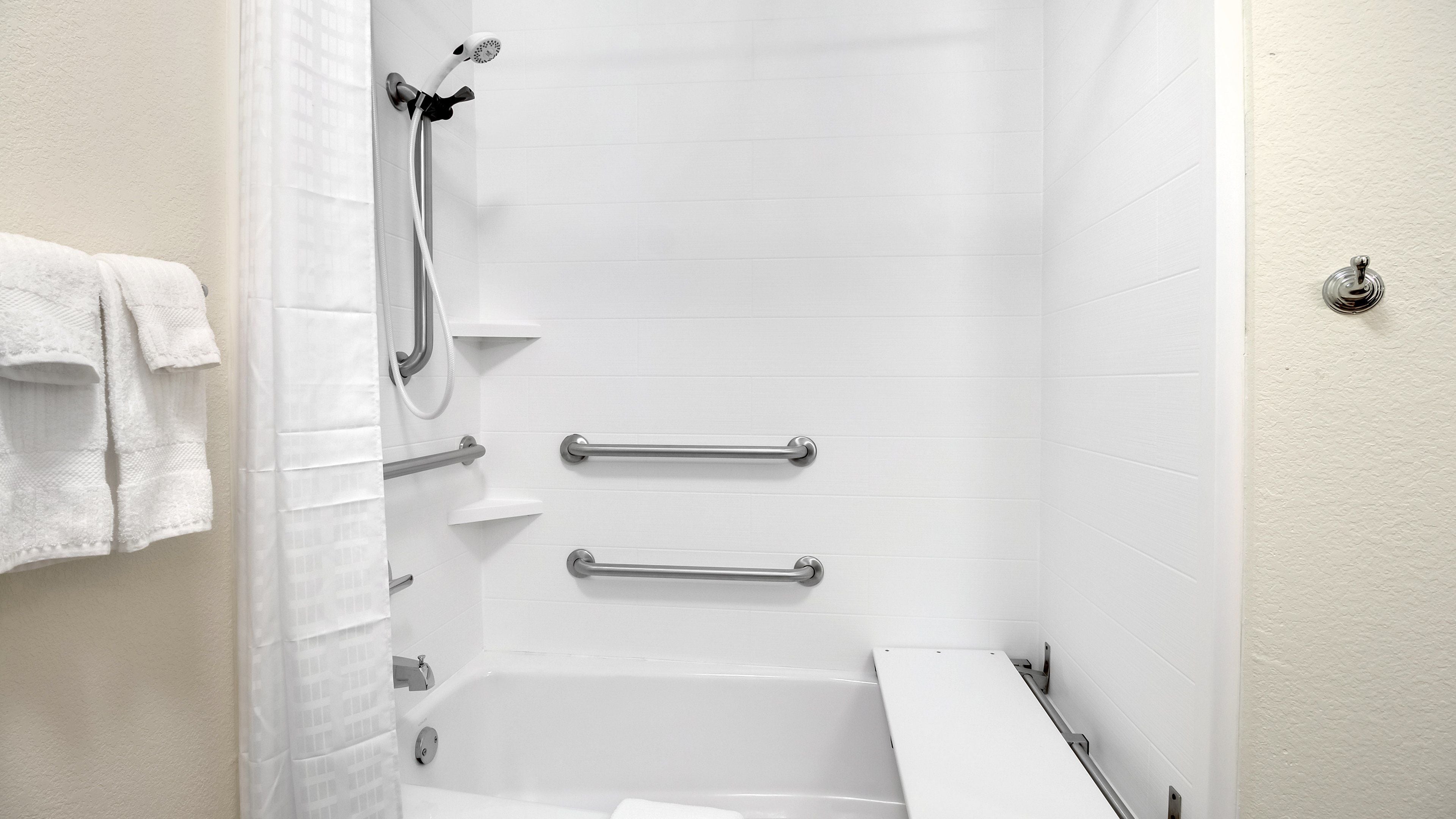 A walk-in shower with a handheld showerhead, grab bars, and a white bathtub.