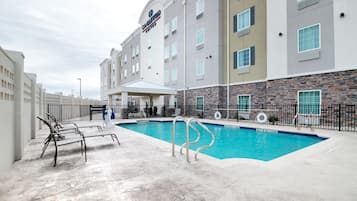 A hotel with a swimming pool, outdoor seating, and a covered area.