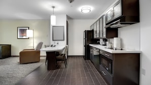 A modern kitchen with dark wood cabinets, a stainless steel refrigerator, and a white countertop. There is a dining area with a round table and chairs.