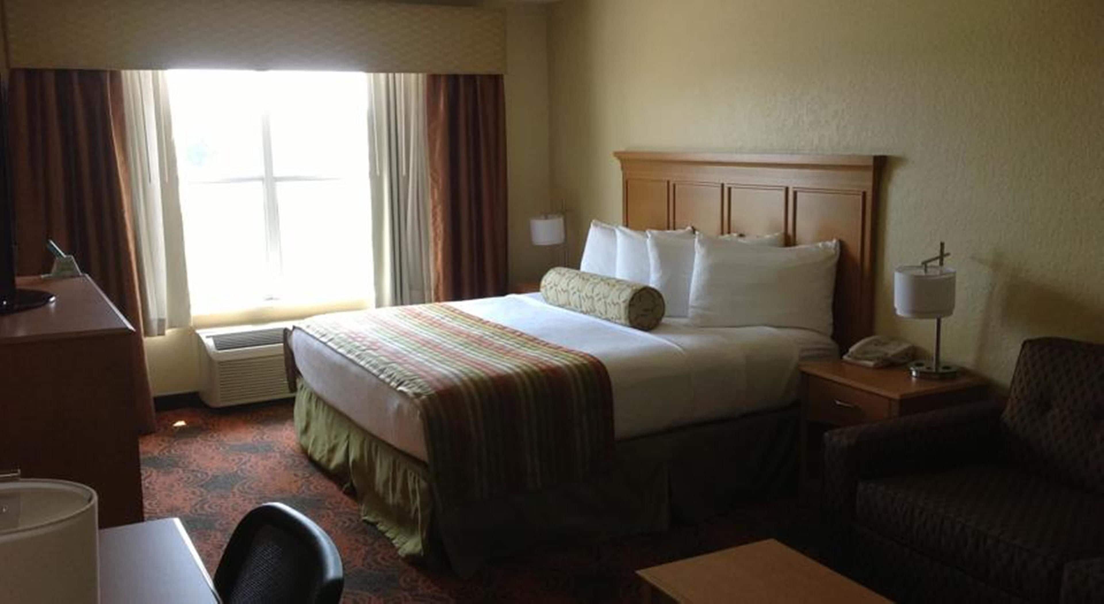 Una habitación de hotel con una cama, un escritorio, una silla, una lámpara y una ventana con cortinas.