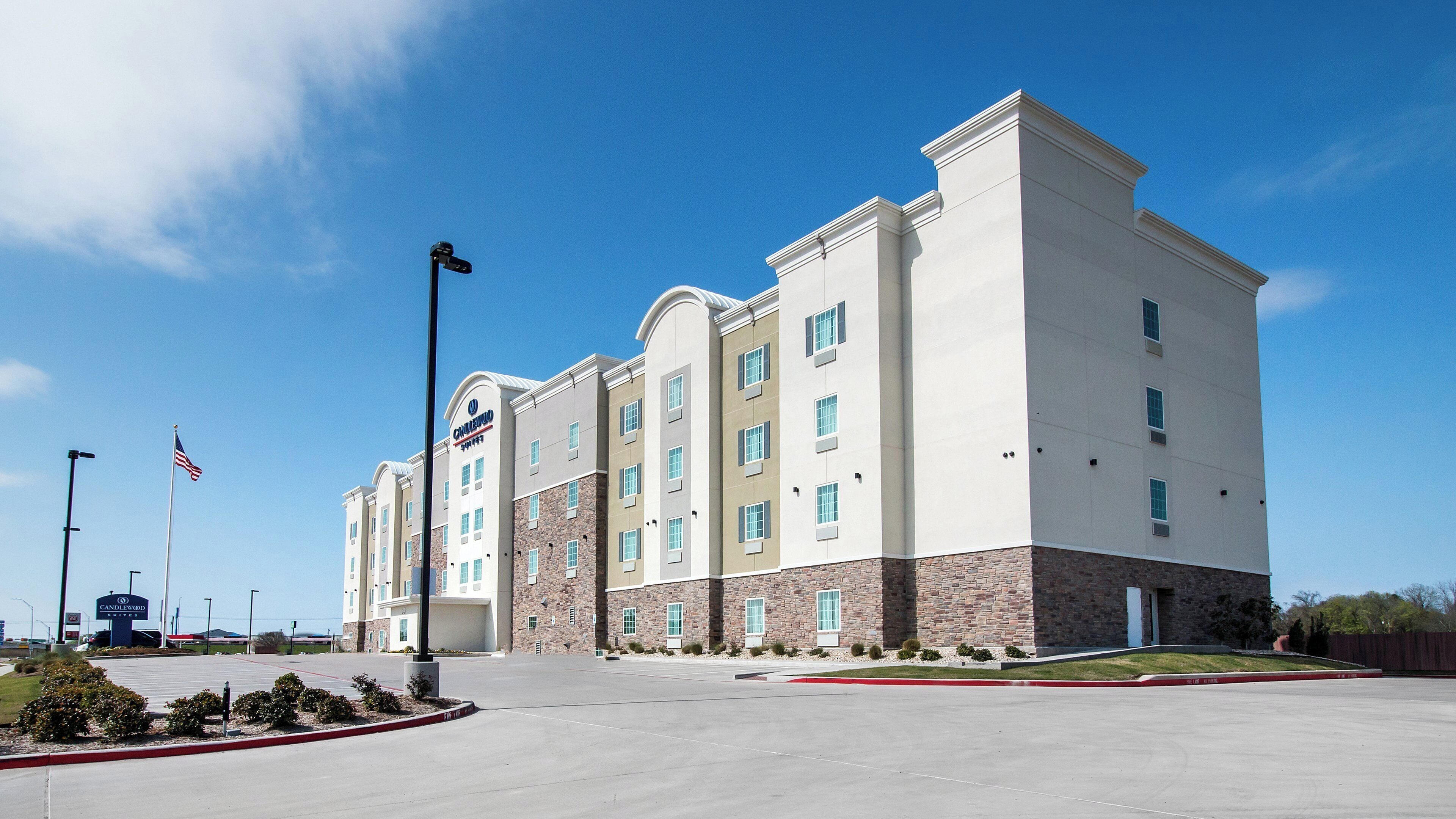 A multi-story hotel with a flat facade, a flagpole with an American flag, and a clear blue sky.