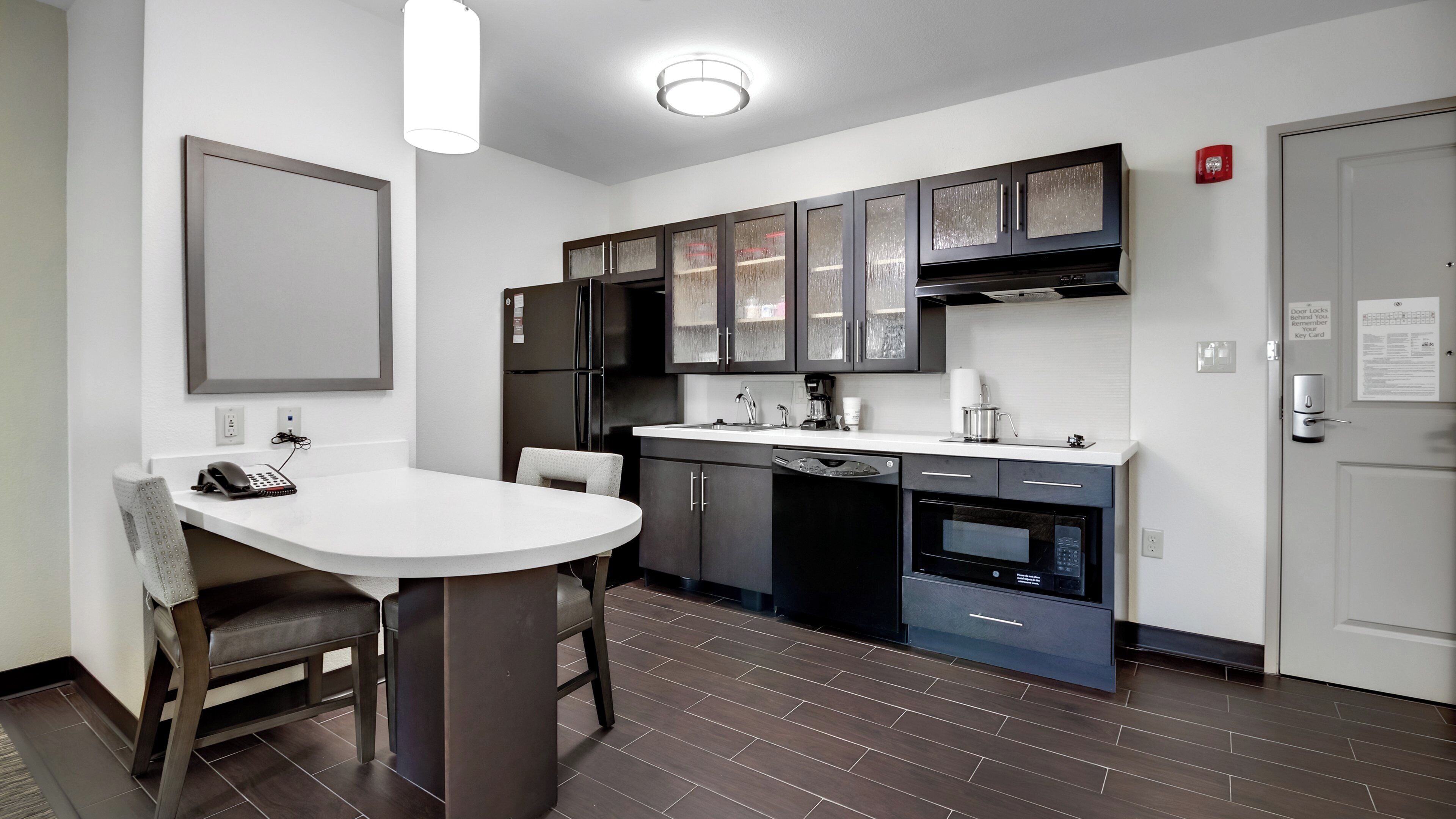 A modern kitchen with dark cabinetry, a white countertop, and a built-in dishwasher.