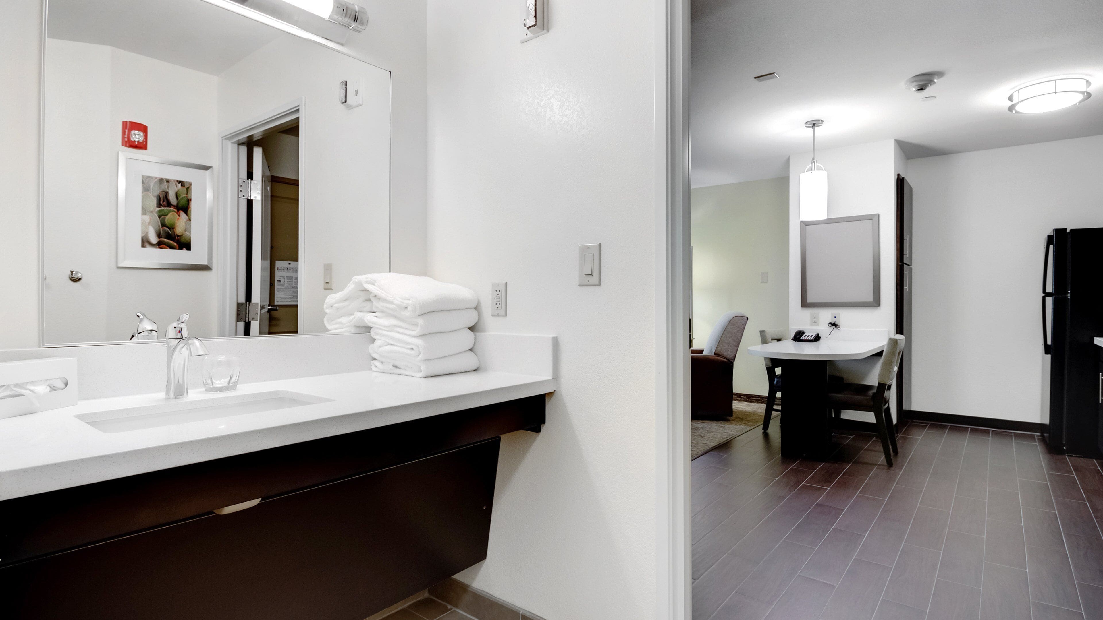 A modern bathroom with a large mirror, two sinks, and a stack of white towels.
