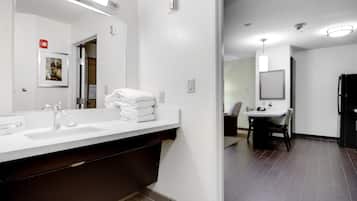 A modern bathroom with a large mirror, two sinks, and a stack of white towels.