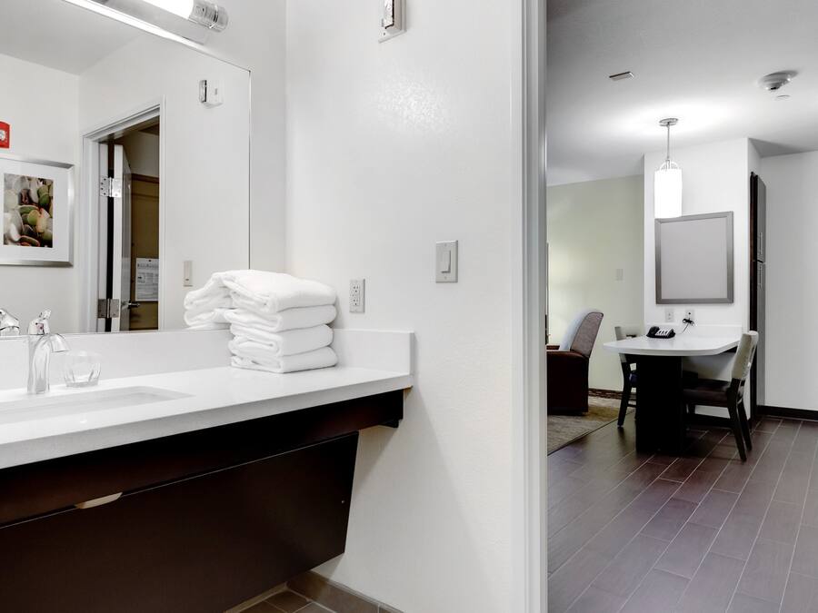 A modern bathroom with a large mirror, two sinks, and a stack of white towels.