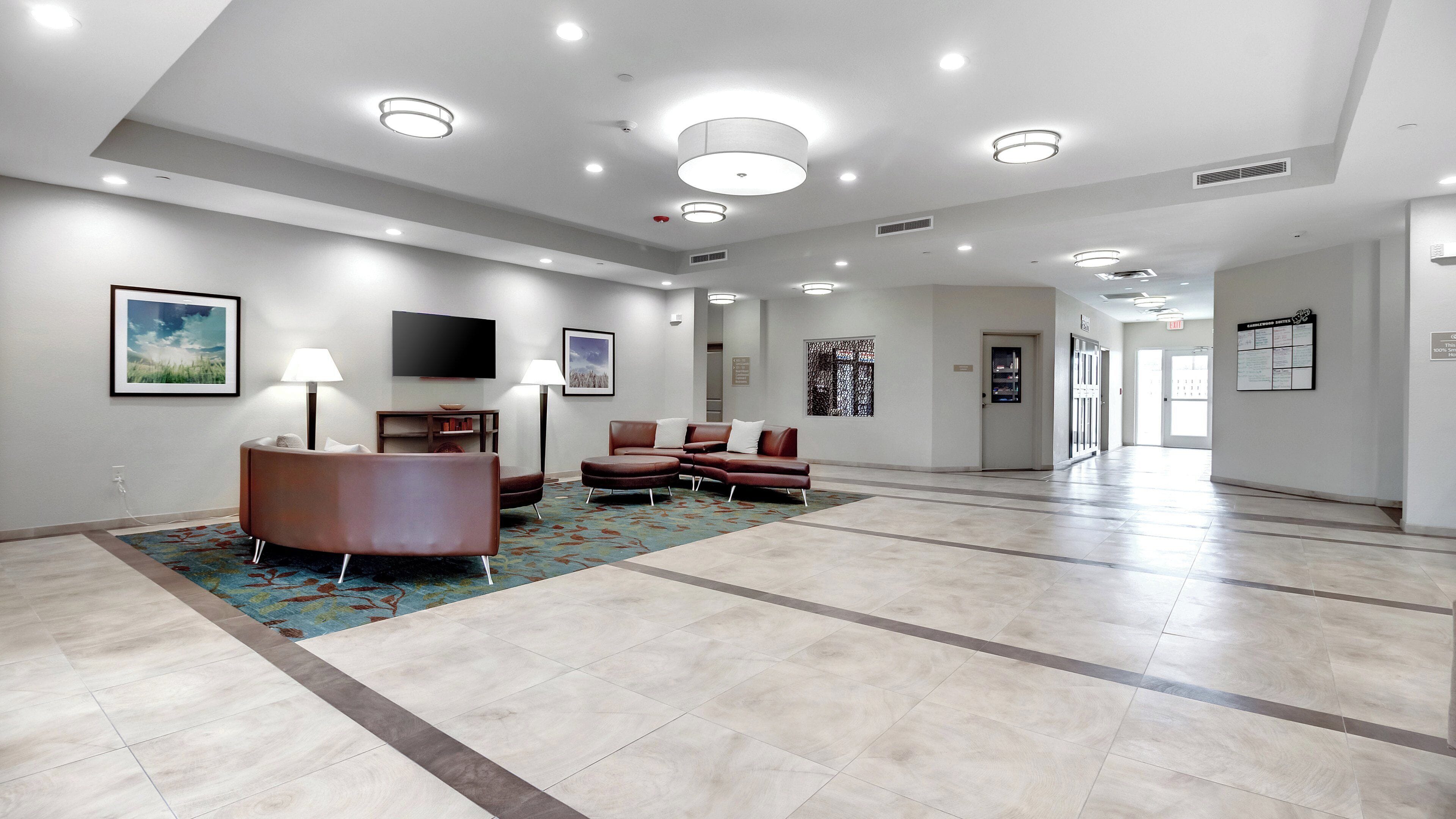 Un hall d’entrée spacieux au design moderne, comprenant un coin salon avec un canapé et des fauteuils en cuir marron, un téléviseur à écran plat fixé au mur et un tapis à motifs sur le sol.