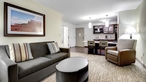 A living room with a sofa, armchair, and coffee table, a kitchen with modern appliances, and a framed picture on the wall.