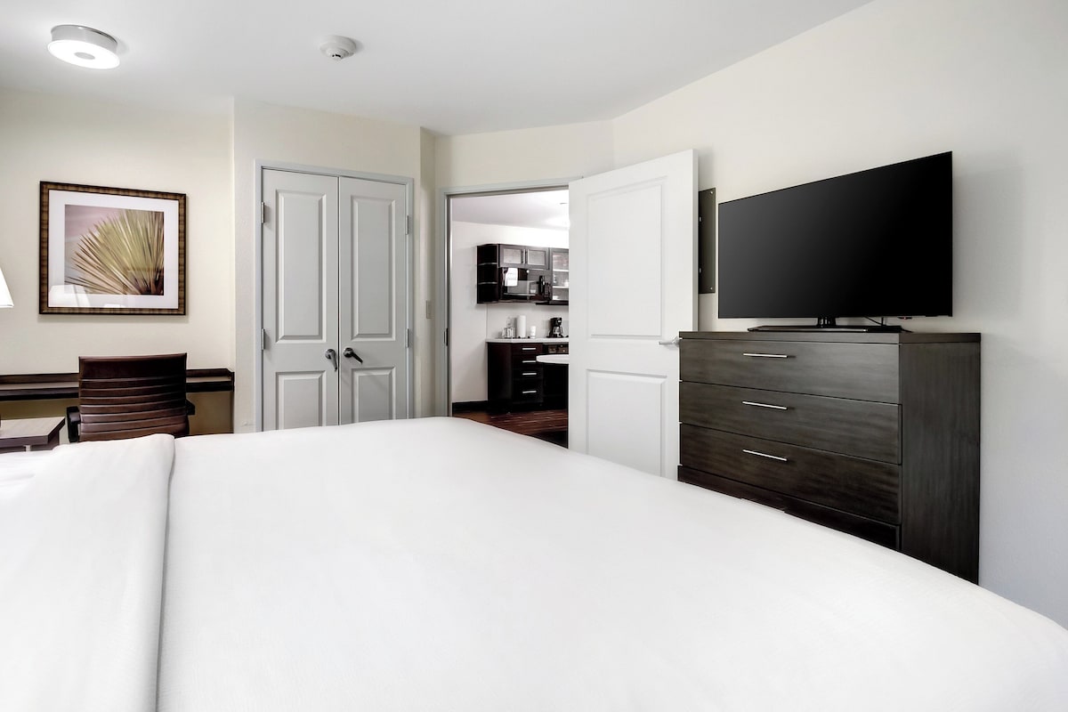 Una habitación de hotel con cama, escritorio, silla, televisor y armario.