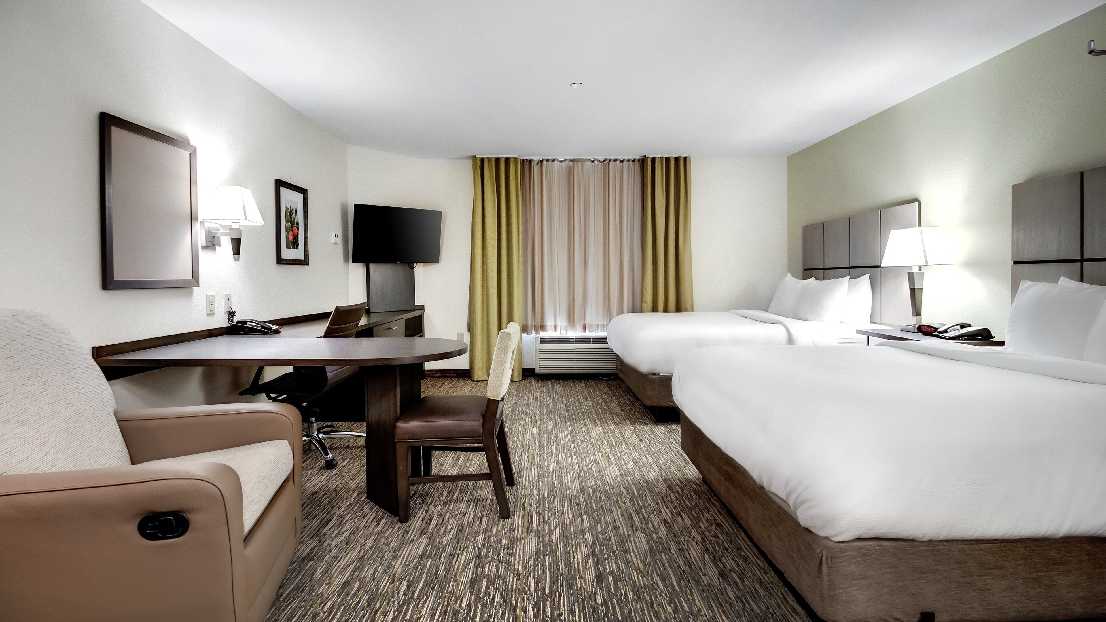 A hotel room with a desk, two beds, a TV, and a window with curtains.