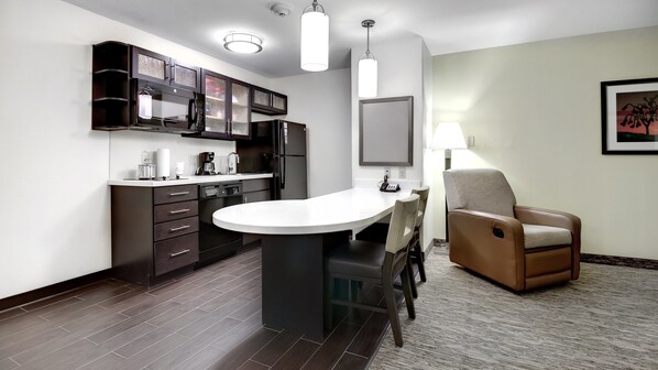 Una cocina moderna con armarios oscuros, una isla central y una zona de comedor con una silla.