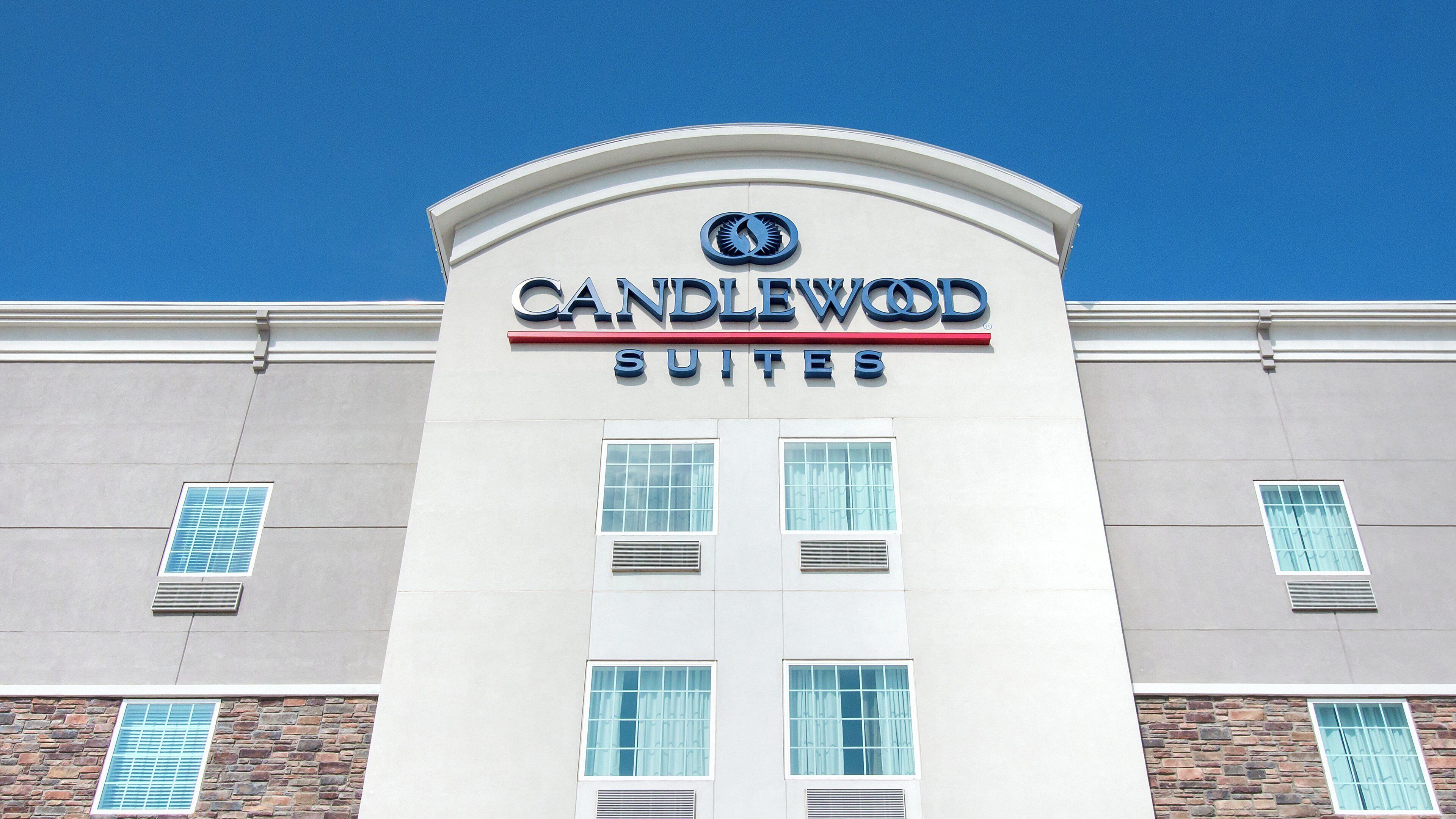 A hotel named 'CANDLEWOOD SUITES' with a modern facade, large windows, and a clear blue sky in the background.