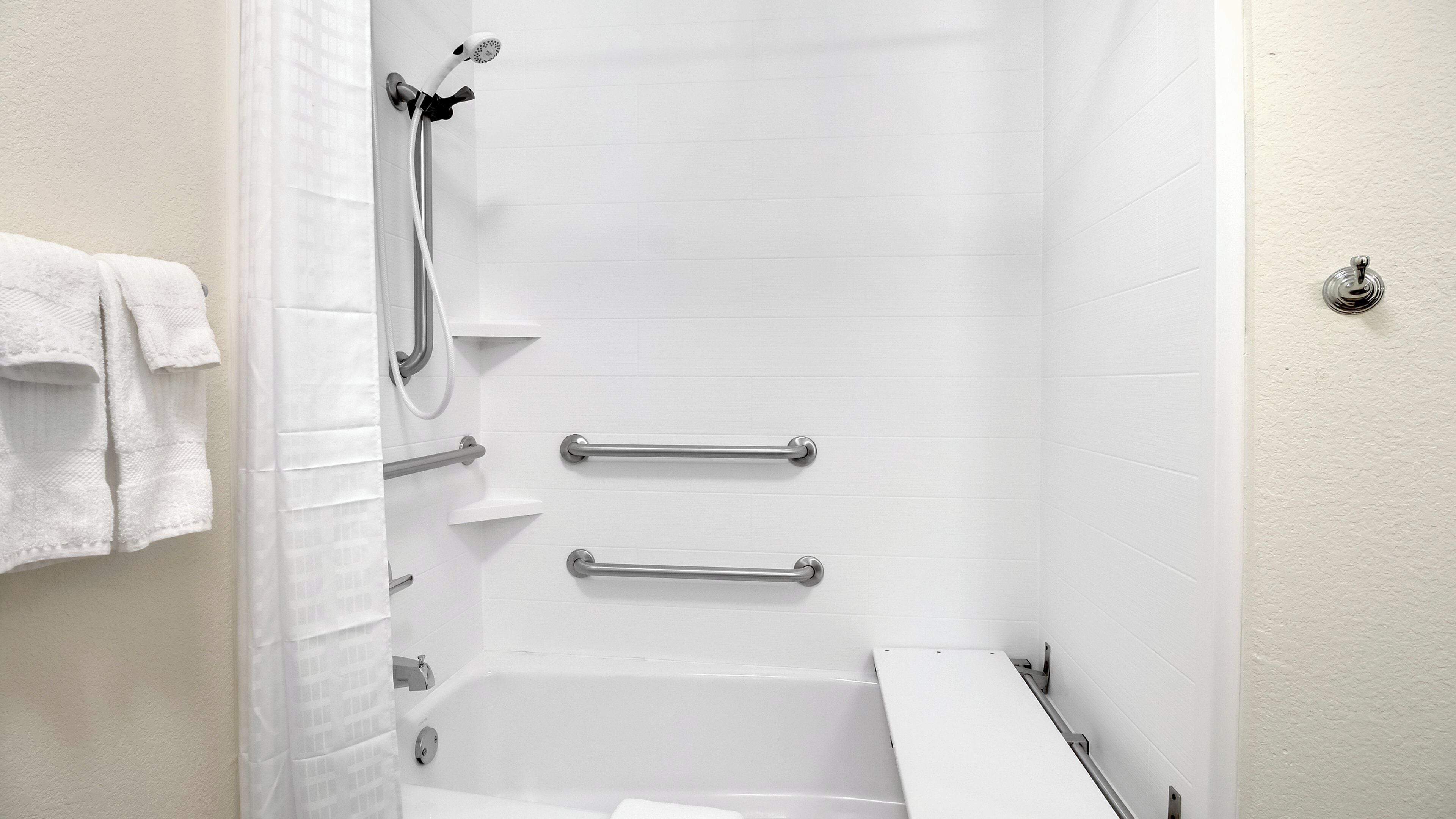 Ein Badezimmer mit einer Badewanne, einer Dusche inklusive Duschbrause und Sicherheitsgriffen.