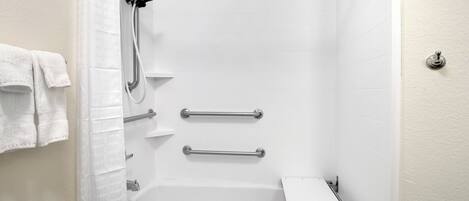 Ein Badezimmer mit einer Badewanne, einer Dusche inklusive Duschbrause und Sicherheitsgriffen.