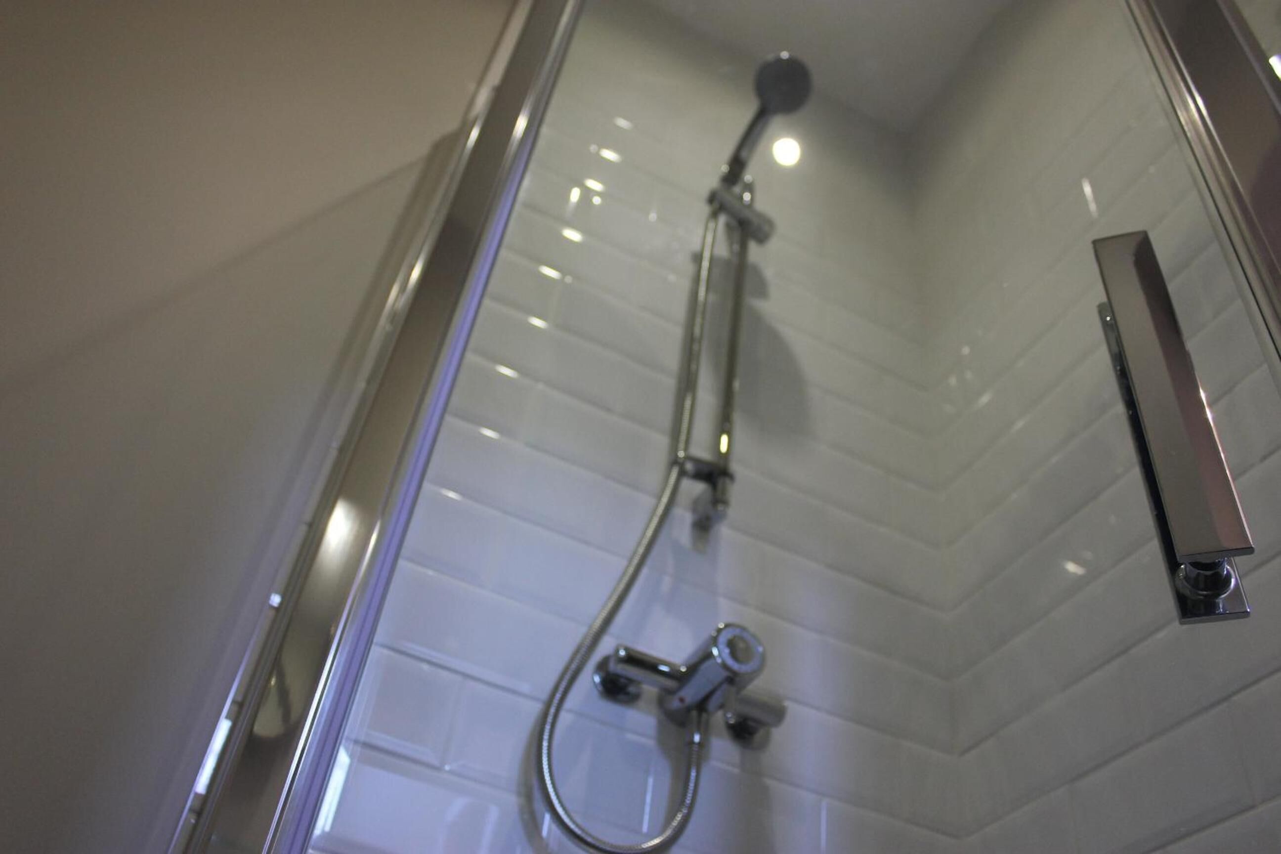 A shower with a handheld showerhead and a wall-mounted faucet.