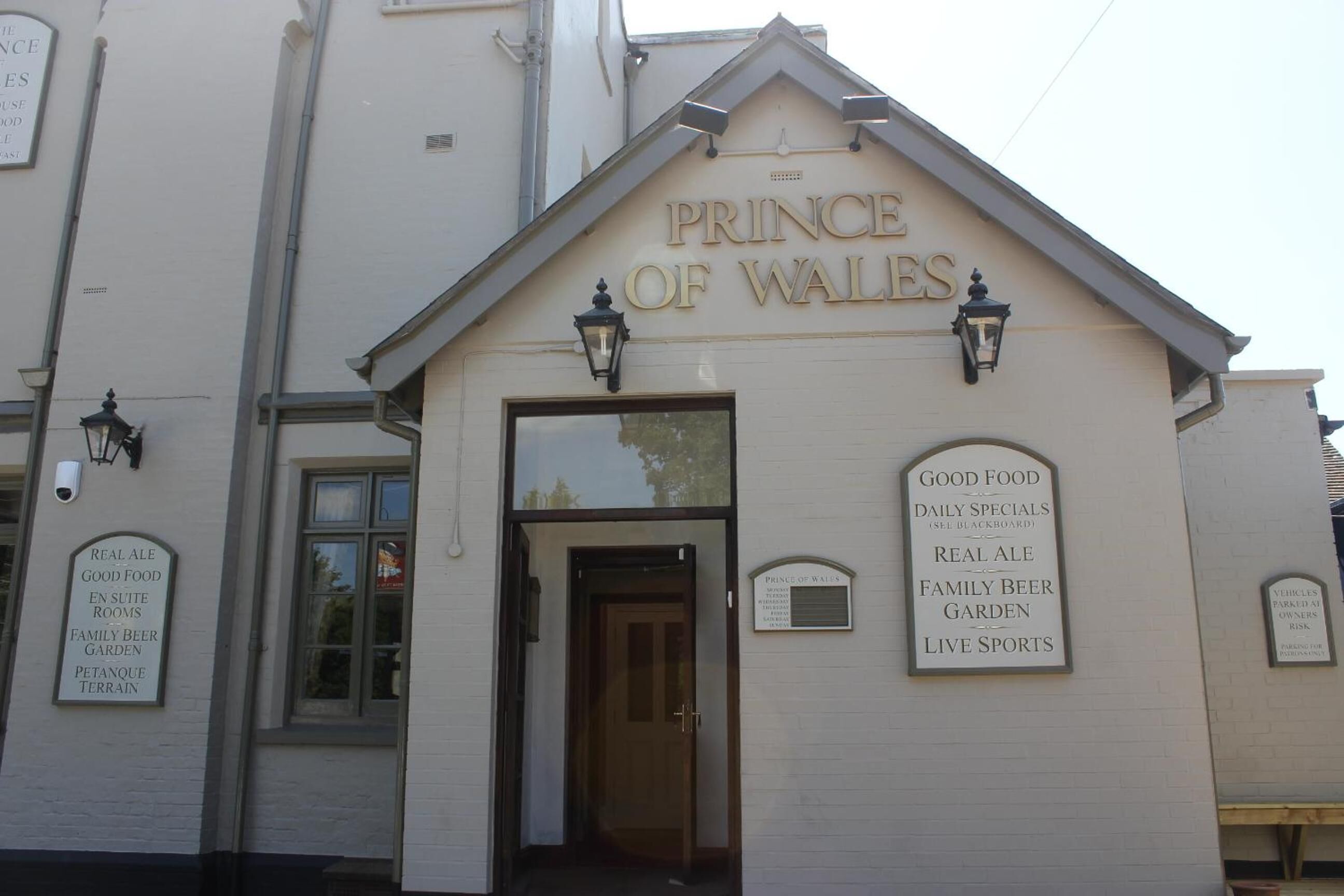 Un edificio con un letrero que dice "PRINCE OF WALES" y otro letrero que enumera comodidades como "BUENA COMIDA", "CERVEZA ARTESANAL" y "DEPORTES EN VIVO".