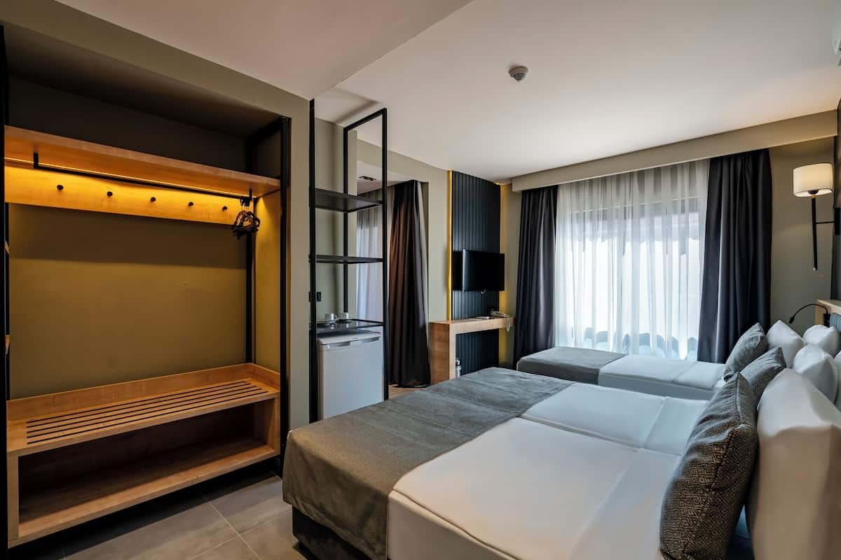 Hotellihuone, jossa on sänky, penkki, televisio ja peili.
