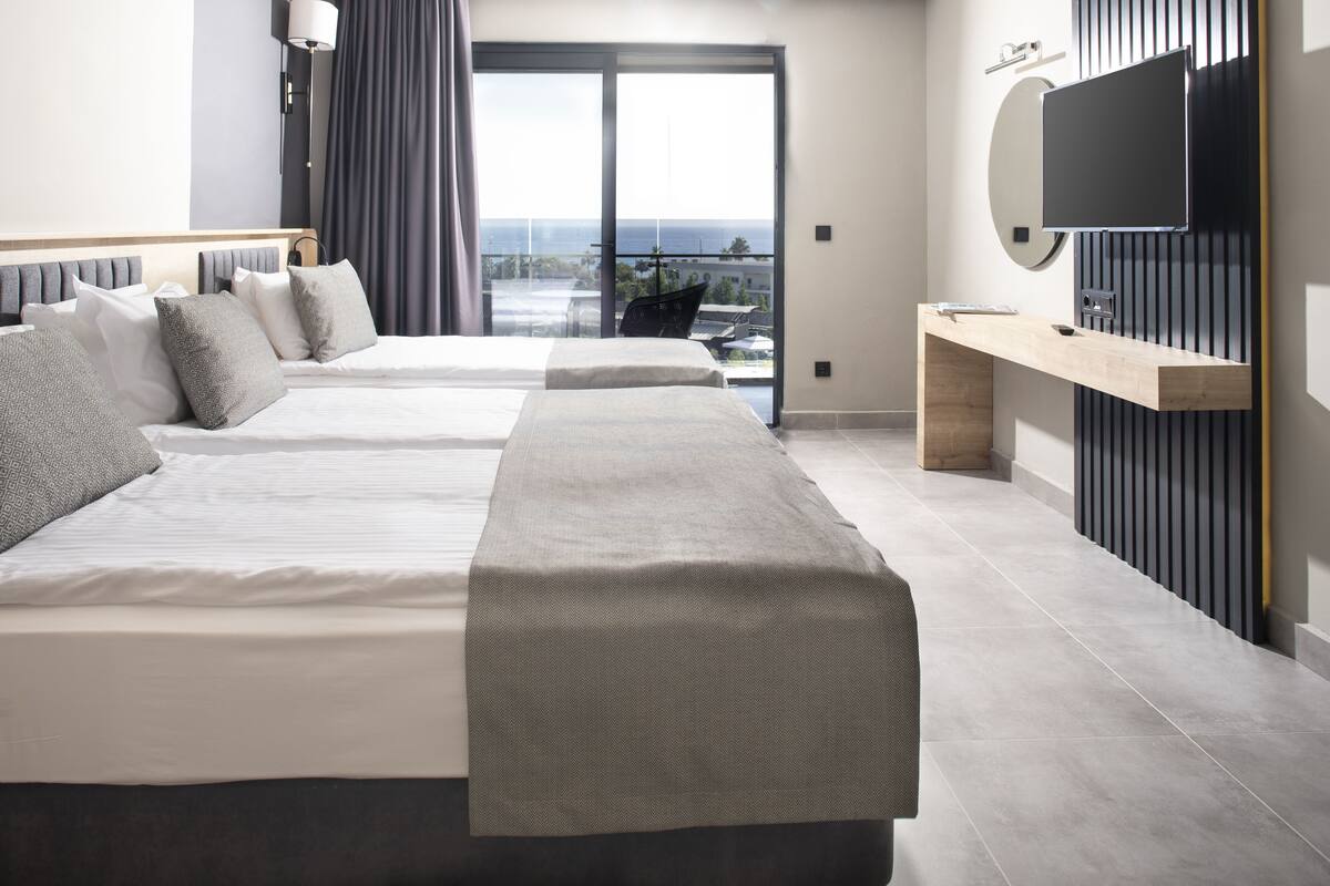 Moderni hotellihuone, jossa on kaksi sänkyä, televisio ja parveke, jolta on näkymä kaupunkiin.