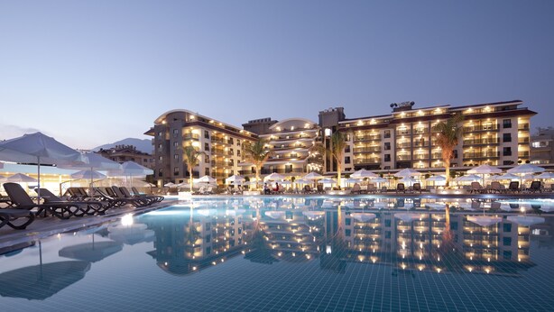 A hotel with a large pool, sun loungers, umbrellas, and a well-lit exterior.
