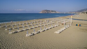 A beach with rows of sun loungers and umbrellas, a flagpole, and a distant mountain.