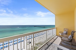 Ein Balkon mit Blick auf einen Strand und einen Steg. Auf dem Balkon stehen Liegestühle und Sonnenschirme.